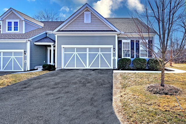view of front of home with driveway, an attached garage, a shingled roof, and a front lawn