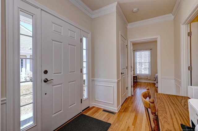 foyer featuring a wainscoted wall, a decorative wall, visible vents, light wood-style floors, and ornamental molding