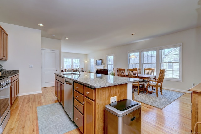 kitchen with a center island with sink, a sink, light stone counters, light wood finished floors, and appliances with stainless steel finishes