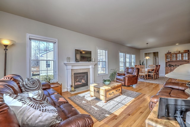 living room featuring a glass covered fireplace, baseboards, and light wood-type flooring
