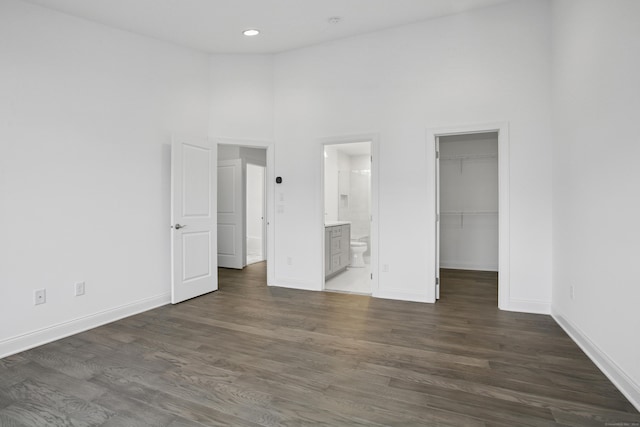 unfurnished bedroom with dark wood-type flooring, a high ceiling, a spacious closet, and baseboards