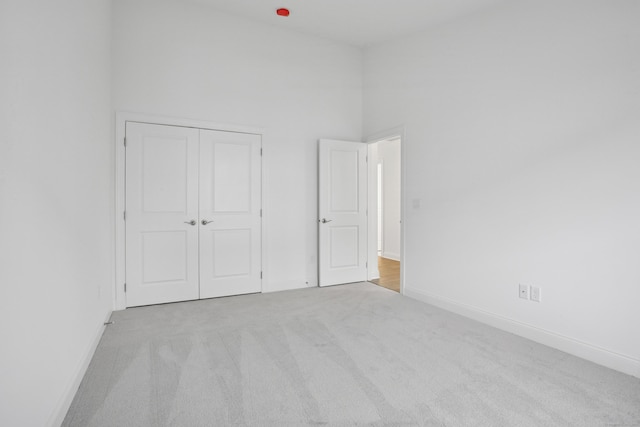 unfurnished bedroom featuring a closet, carpet flooring, a towering ceiling, and baseboards