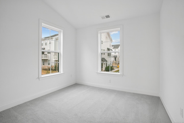 empty room with visible vents, vaulted ceiling, light carpet, and baseboards