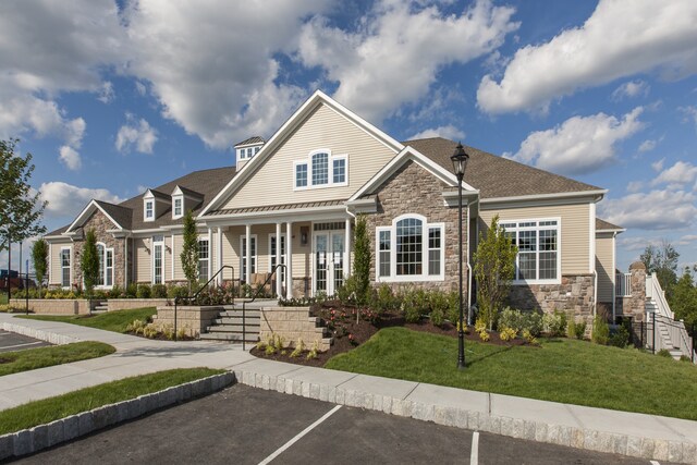 view of front of house featuring uncovered parking, stone siding, covered porch, and a front lawn