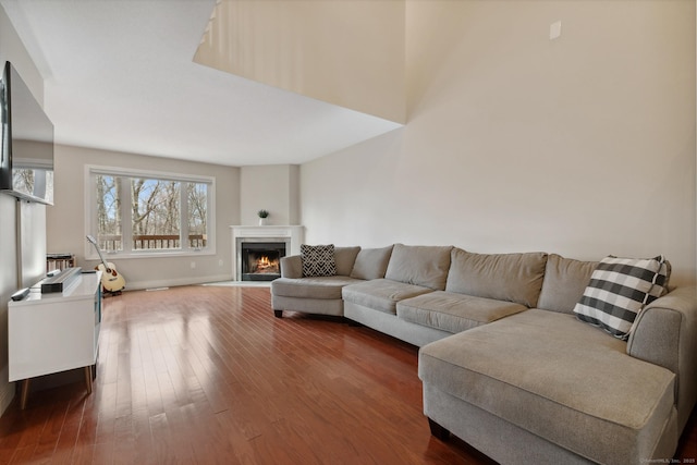 living room featuring baseboards, a fireplace with flush hearth, and dark wood-style flooring