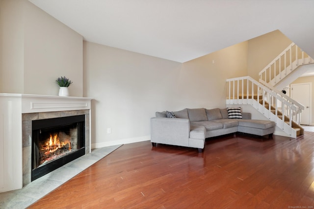 unfurnished living room featuring stairway, wood finished floors, baseboards, and a tile fireplace