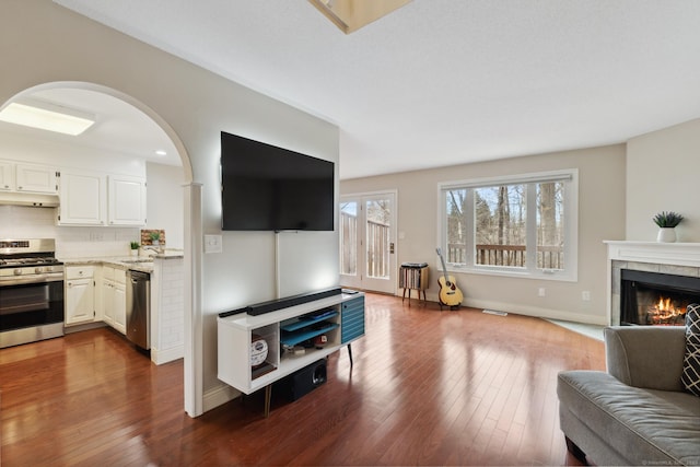 living room with visible vents, dark wood-type flooring, a tiled fireplace, arched walkways, and baseboards