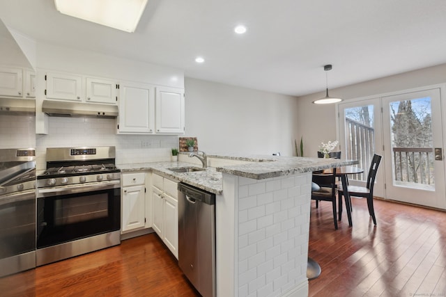 kitchen with under cabinet range hood, a sink, dark wood finished floors, appliances with stainless steel finishes, and a peninsula