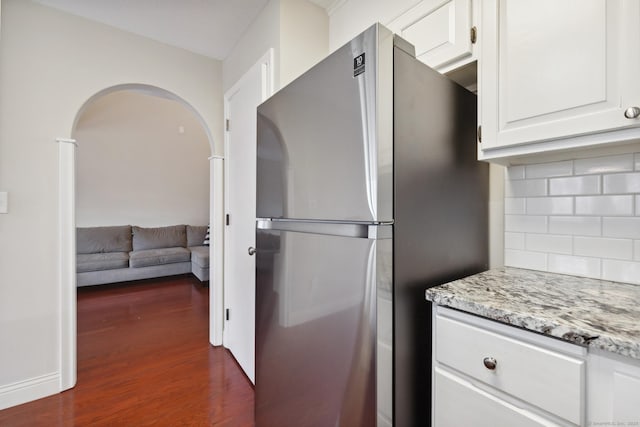 kitchen featuring light stone counters, dark wood-style floors, freestanding refrigerator, white cabinets, and tasteful backsplash