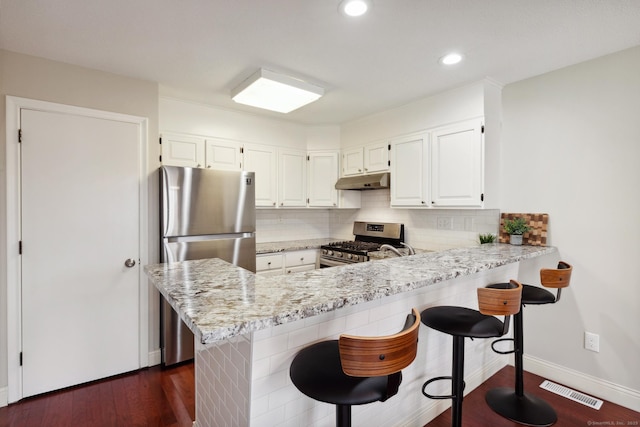 kitchen featuring visible vents, under cabinet range hood, dark wood-style floors, appliances with stainless steel finishes, and decorative backsplash