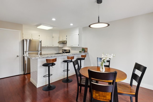 kitchen with dark wood finished floors, a peninsula, appliances with stainless steel finishes, under cabinet range hood, and backsplash