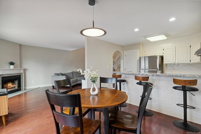 dining room featuring baseboards, recessed lighting, a warm lit fireplace, light wood-style floors, and arched walkways