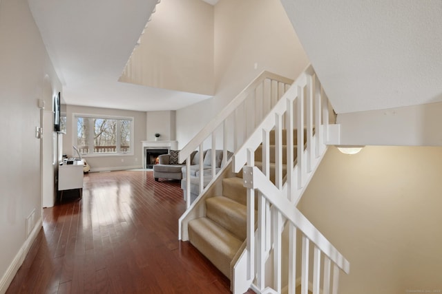 stairway with visible vents, a warm lit fireplace, baseboards, and wood-type flooring