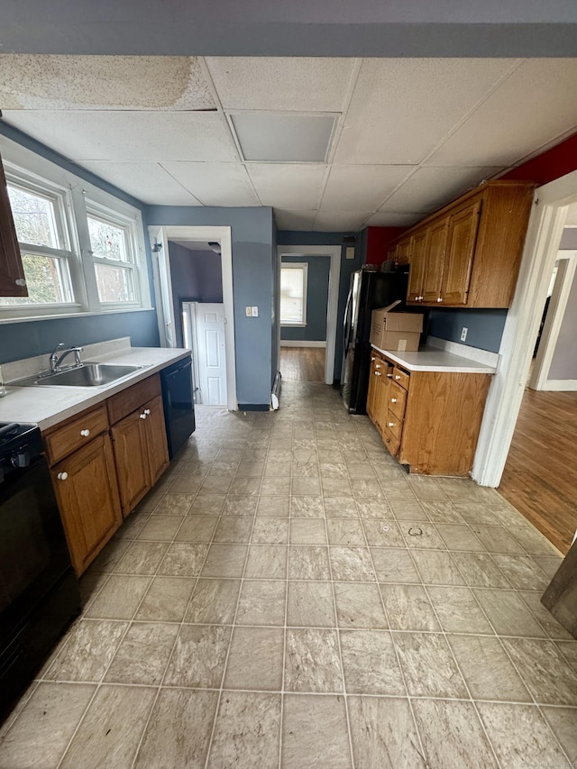 kitchen featuring black appliances, a sink, brown cabinetry, light countertops, and a paneled ceiling