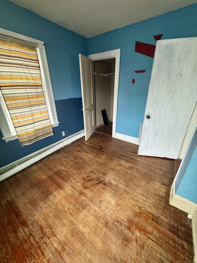 unfurnished bedroom with baseboard heating, a closet, baseboards, and wood-type flooring