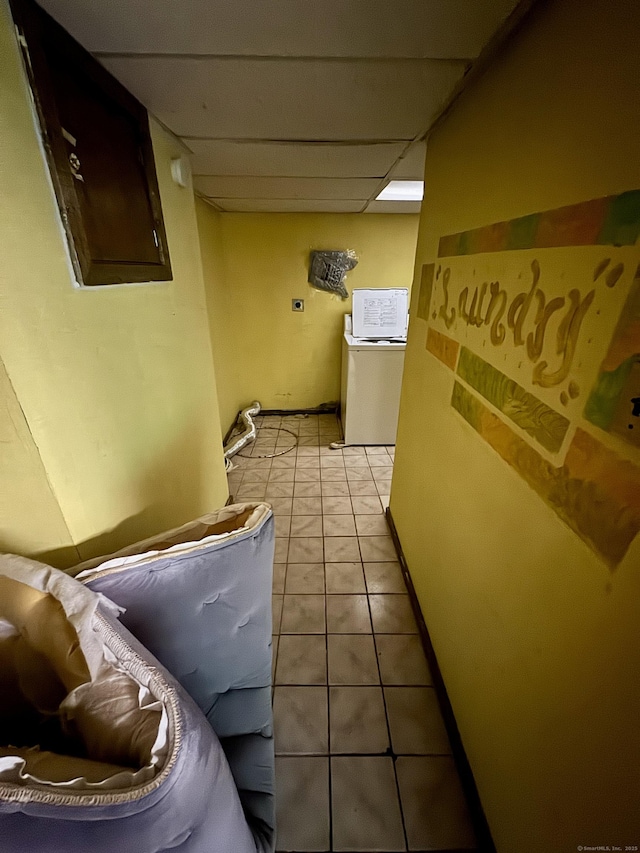 hall with light tile patterned floors, a drop ceiling, washer / clothes dryer, and baseboards