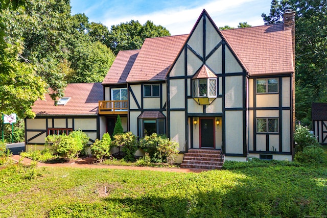 tudor house featuring a front yard, a chimney, and stucco siding