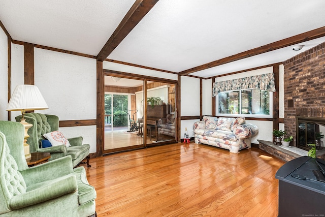 living area featuring a fireplace, beamed ceiling, wood finished floors, and a textured ceiling