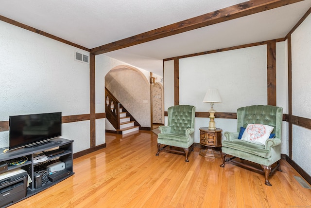 living area featuring stairway, wood finished floors, visible vents, beam ceiling, and arched walkways