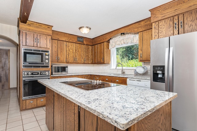 kitchen with a center island, light tile patterned floors, brown cabinets, black appliances, and a sink