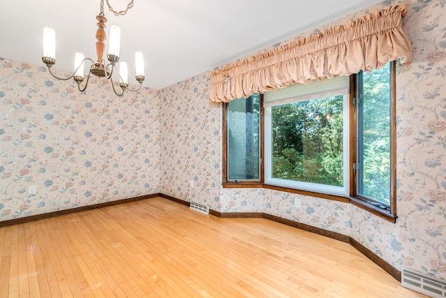 spare room featuring wallpapered walls, an inviting chandelier, visible vents, and hardwood / wood-style floors