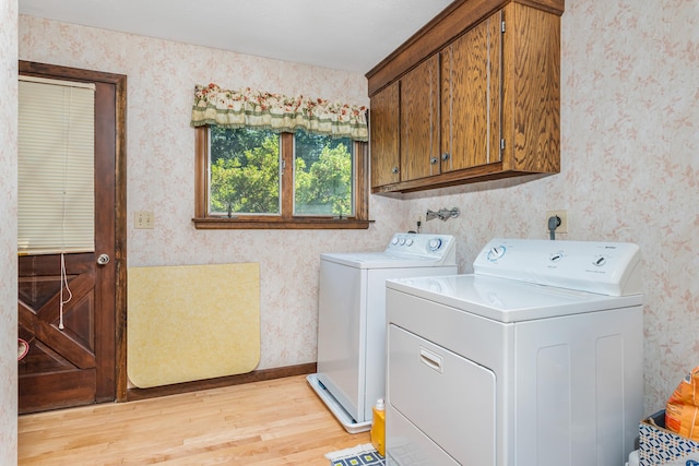 washroom featuring baseboards, light wood finished floors, wallpapered walls, cabinet space, and washer and dryer