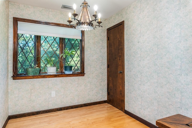 spare room with visible vents, an inviting chandelier, wood finished floors, and wallpapered walls