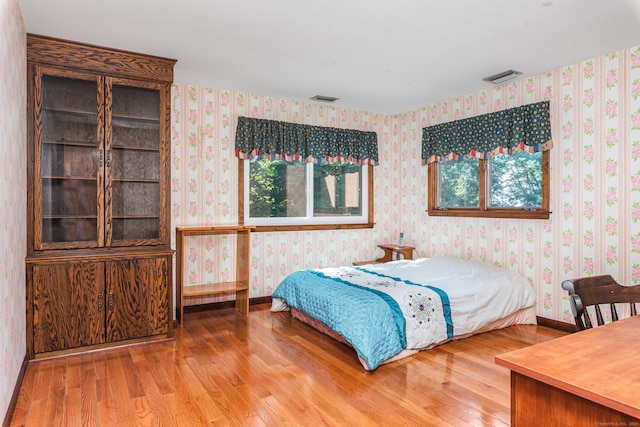 bedroom featuring visible vents, wallpapered walls, and wood finished floors