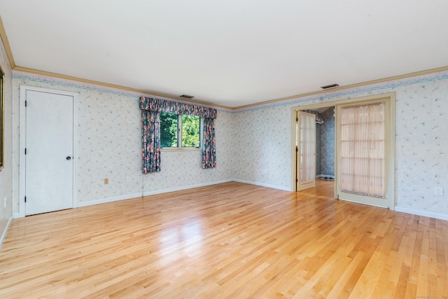 empty room with wood finished floors, baseboards, visible vents, wallpapered walls, and crown molding