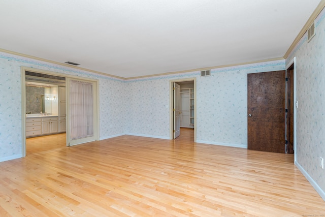unfurnished room with wallpapered walls, crown molding, and light wood-style flooring
