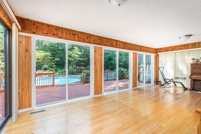 interior space with light wood finished floors, visible vents, a textured ceiling, and wooden walls