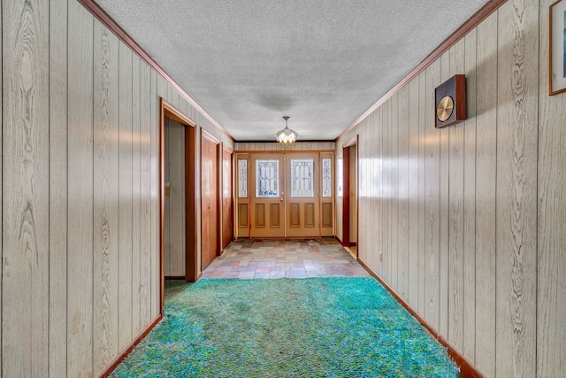 interior space with a textured ceiling, carpet floors, ornamental molding, and wooden walls