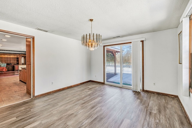 spare room featuring visible vents, a notable chandelier, a textured ceiling, and wood finished floors