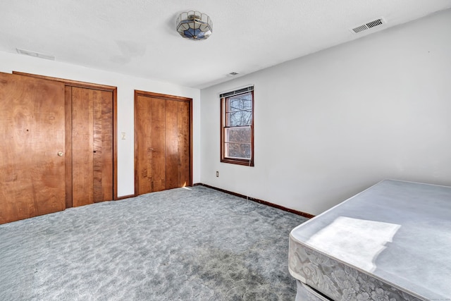 carpeted bedroom with baseboards, a textured ceiling, visible vents, and multiple closets