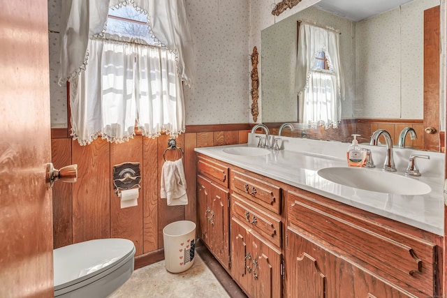 bathroom with wainscoting, a sink, toilet, and wallpapered walls