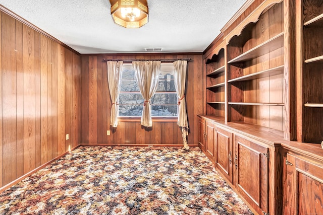 unfurnished office featuring wooden walls, baseboards, visible vents, carpet, and a textured ceiling