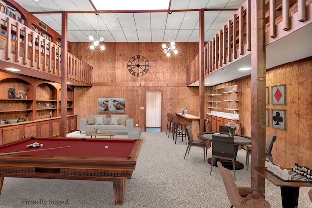 playroom with an inviting chandelier, wooden walls, a high ceiling, and carpet flooring