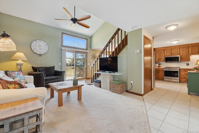 living room with baseboards, ceiling fan, light colored carpet, stairs, and light tile patterned floors