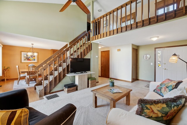 living room featuring visible vents, baseboards, stairs, ceiling fan with notable chandelier, and a high ceiling