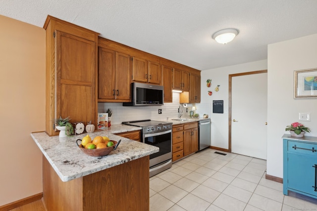 kitchen with brown cabinetry, visible vents, a peninsula, a sink, and stainless steel appliances