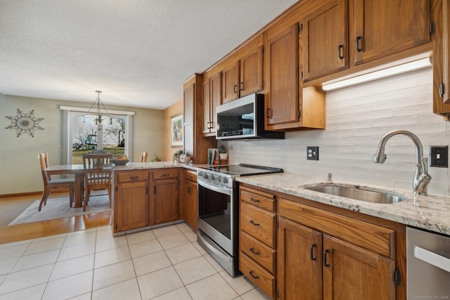 kitchen with a sink, stainless steel appliances, a peninsula, and brown cabinetry