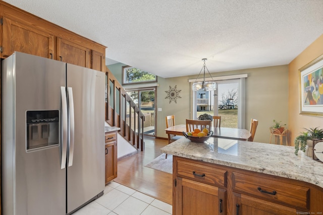 kitchen featuring light stone counters, hanging light fixtures, stainless steel refrigerator with ice dispenser, a textured ceiling, and brown cabinets