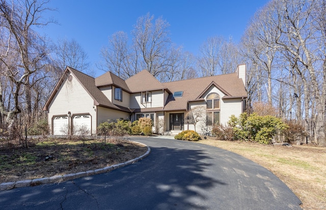 view of front of property featuring roof with shingles, an attached garage, driveway, and a chimney