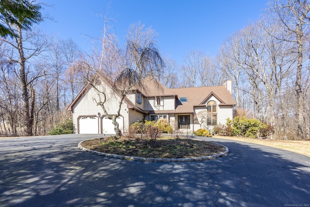 view of front facade with driveway, a chimney, and an attached garage