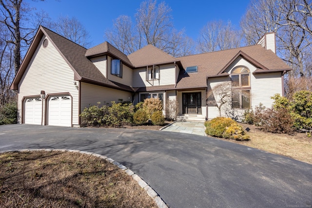 view of front of house featuring a chimney, driveway, a shingled roof, and a garage