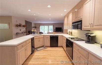 kitchen with light brown cabinetry, light wood-type flooring, light countertops, black appliances, and a sink