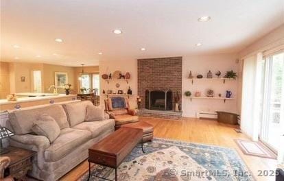 living area with a wealth of natural light, a brick fireplace, wood finished floors, and a baseboard radiator