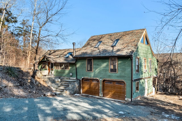 chalet / cabin featuring a garage, driveway, and roof with shingles