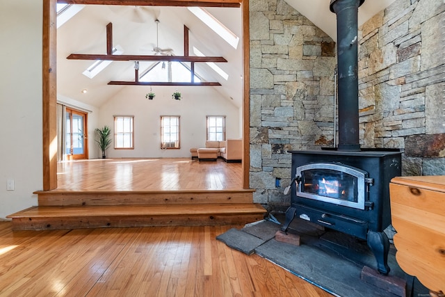 living area featuring a wood stove, hardwood / wood-style flooring, ceiling fan, and high vaulted ceiling