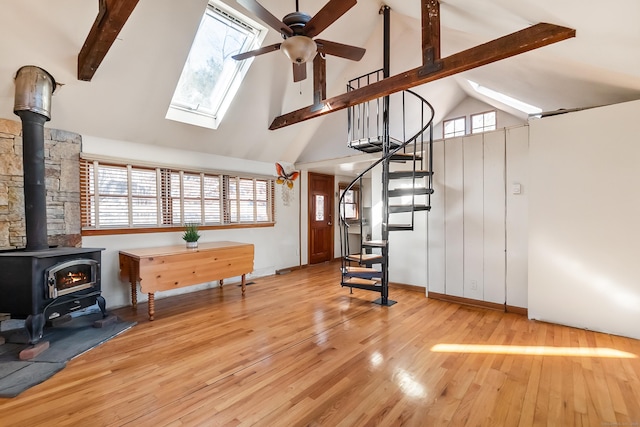 living area featuring a skylight, wood finished floors, a ceiling fan, stairs, and a wood stove